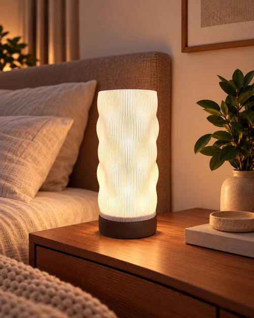 Lámpara Bruma con base Café, encendida en luz cálida sobre la mesa de noche, junto a la cama