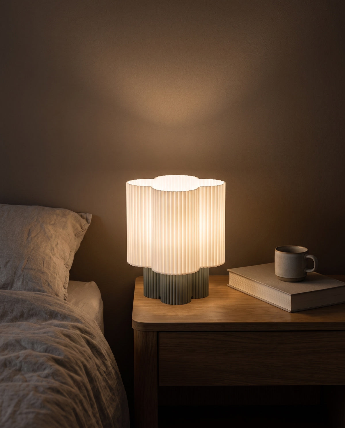Lámpara Trébol con base Salvia, encendida en una mesa de noche junto a la cama