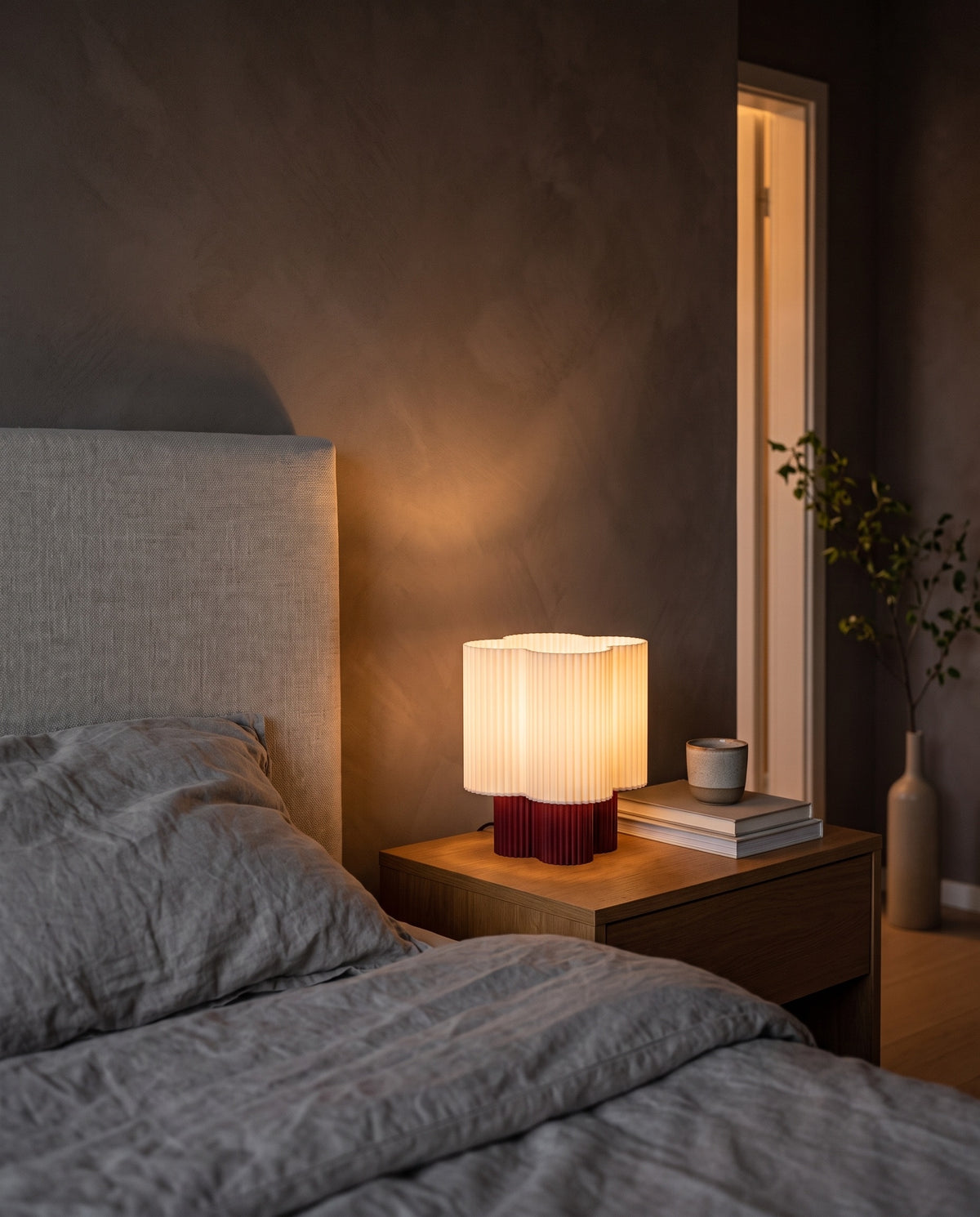 Lámpara Trébol con base Amarena, encendida en una mesa de noche junto a la cama