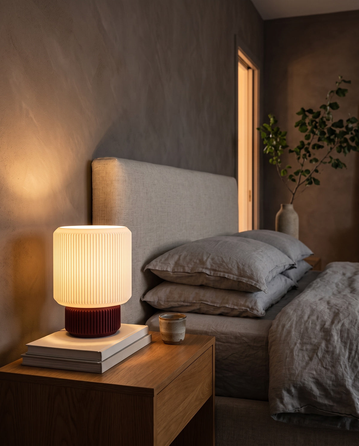 Lámpara Ágora con base Amarena, encendida en una mesa de noche junto a la cama